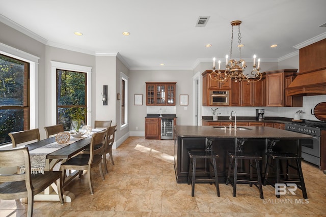 kitchen with appliances with stainless steel finishes, sink, an island with sink, beverage cooler, and ornamental molding