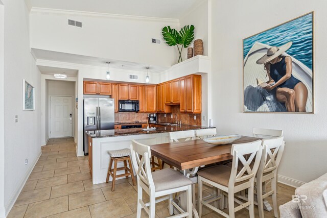 kitchen with stainless steel refrigerator with ice dispenser, kitchen peninsula, dark stone counters, decorative backsplash, and light tile patterned flooring