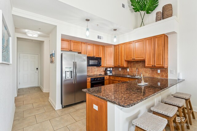 kitchen featuring sink, kitchen peninsula, dark stone countertops, decorative light fixtures, and black appliances