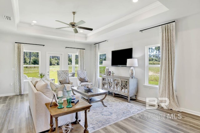 living room with ceiling fan, ornamental molding, a tray ceiling, and light hardwood / wood-style flooring