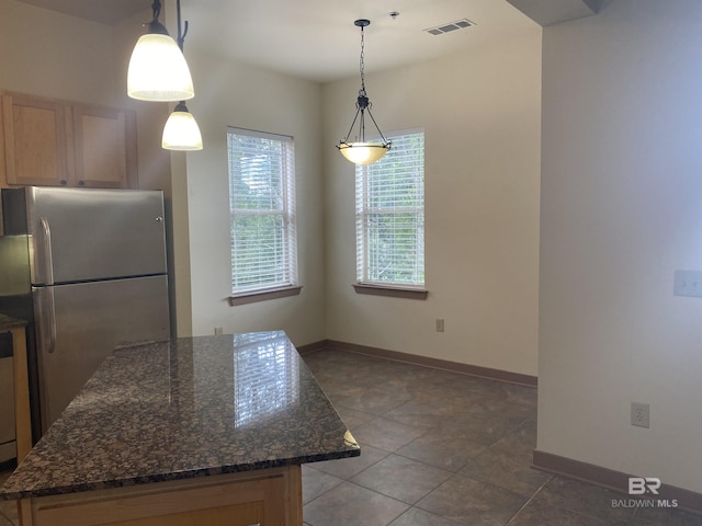 kitchen featuring decorative light fixtures, dark stone counters, stainless steel refrigerator, and dark tile patterned flooring