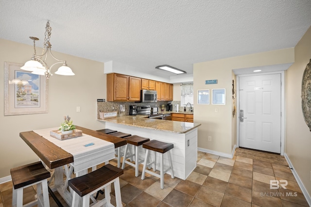 kitchen featuring tasteful backsplash, brown cabinets, a peninsula, stainless steel appliances, and a sink