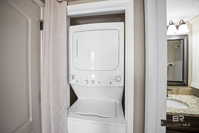 washroom featuring a sink, stacked washer and dryer, laundry area, and a textured ceiling