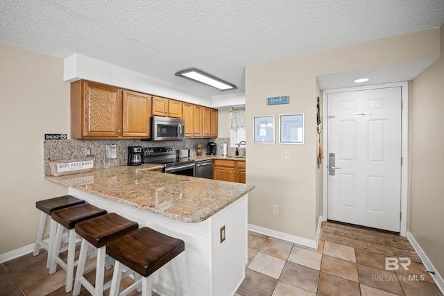 kitchen with a kitchen bar, a sink, tasteful backsplash, appliances with stainless steel finishes, and a peninsula