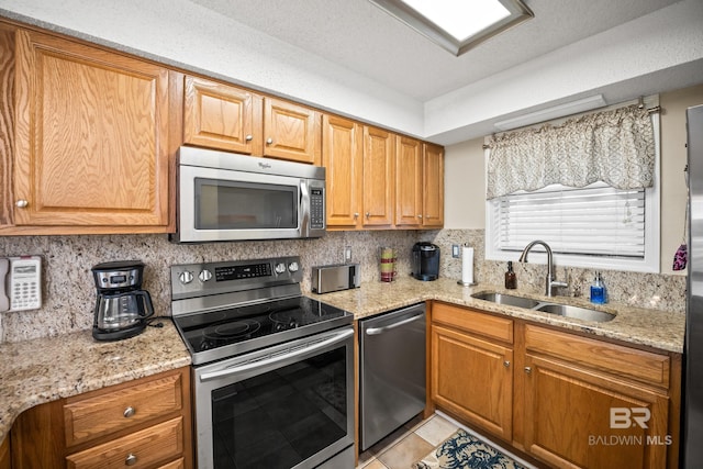 kitchen with light stone countertops, a sink, appliances with stainless steel finishes, tasteful backsplash, and brown cabinets