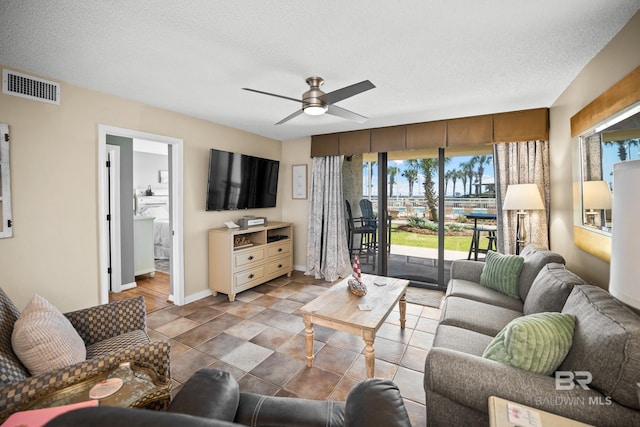 living room featuring visible vents, baseboards, a textured ceiling, and a ceiling fan