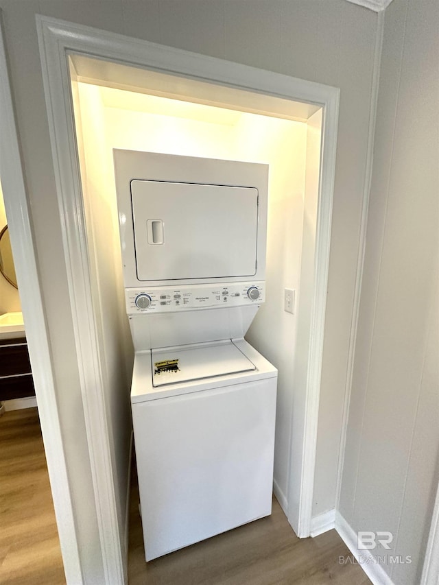 clothes washing area with stacked washer and dryer and hardwood / wood-style flooring