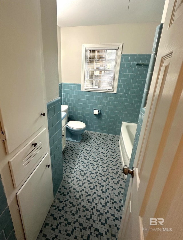 bathroom featuring a tub to relax in, toilet, and tile walls