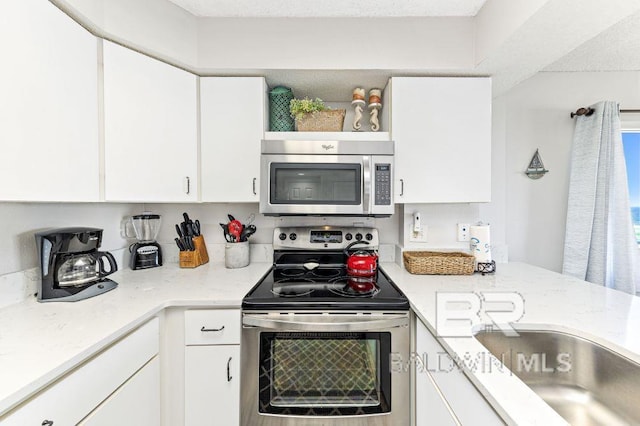 kitchen with white cabinets, sink, light stone countertops, a textured ceiling, and appliances with stainless steel finishes