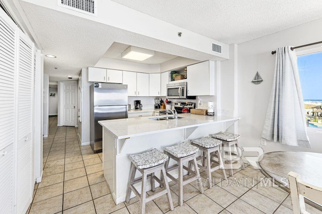 kitchen featuring sink, kitchen peninsula, a breakfast bar, white cabinets, and appliances with stainless steel finishes