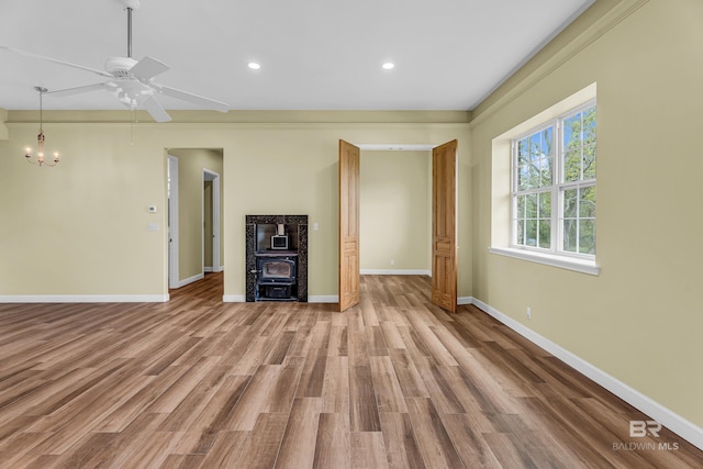 unfurnished living room with baseboards, a wood stove, recessed lighting, wood finished floors, and ceiling fan with notable chandelier