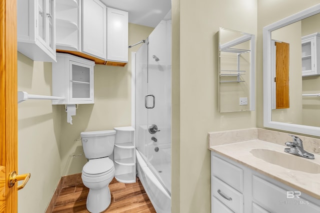 full bath with baseboards, toilet, vanity, wood finished floors, and shower / bath combination with glass door