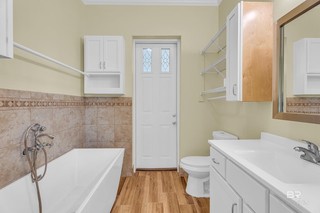 full bath with a bath, vanity, toilet, wood finished floors, and tile walls