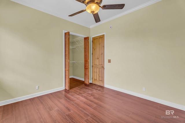 unfurnished bedroom with crown molding, wood finished floors, baseboards, and a closet