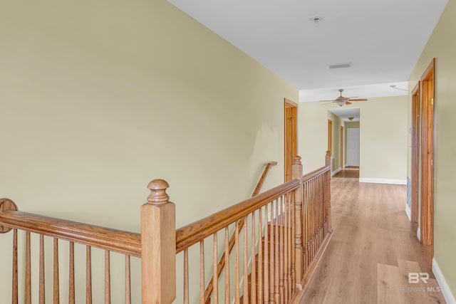 hallway featuring light wood-style floors, visible vents, baseboards, and an upstairs landing