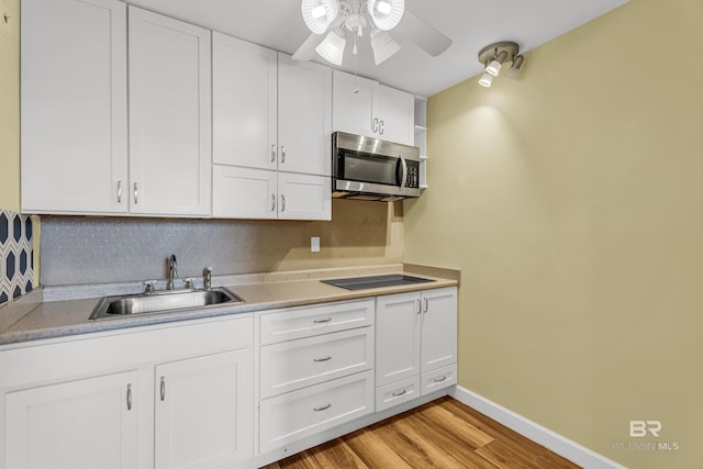 kitchen with light wood-type flooring, a ceiling fan, stainless steel microwave, a sink, and black electric cooktop