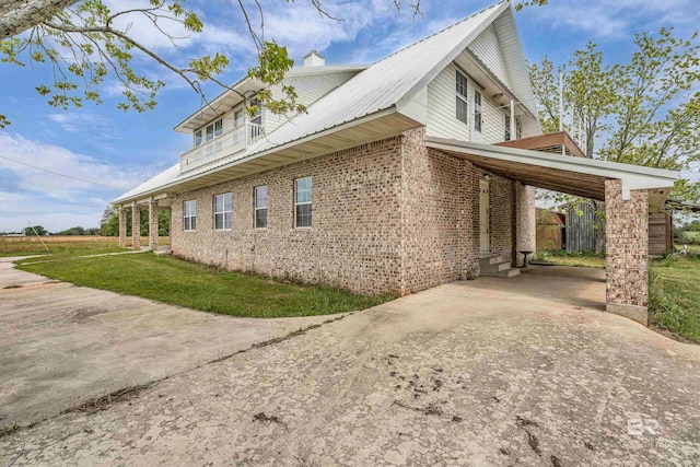 view of side of home with a yard, metal roof, a chimney, brick siding, and driveway