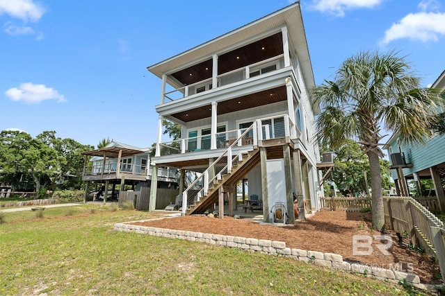 back of house featuring board and batten siding, a lawn, stairway, a balcony, and a fenced backyard