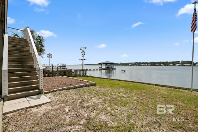view of yard featuring a boat dock, stairway, boat lift, fence, and a water view
