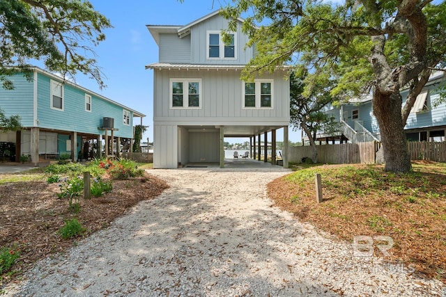 coastal home with board and batten siding, fence, driveway, and a carport