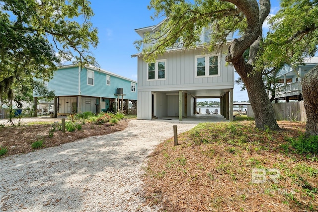 coastal inspired home with dirt driveway, fence, board and batten siding, and a carport