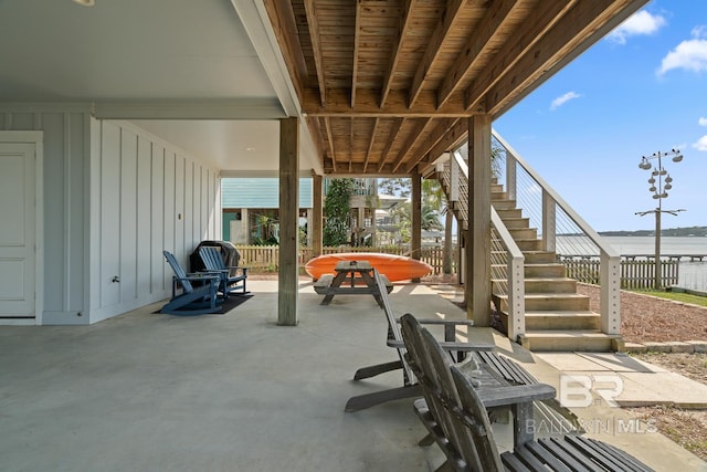 view of patio with fence, a water view, and stairway