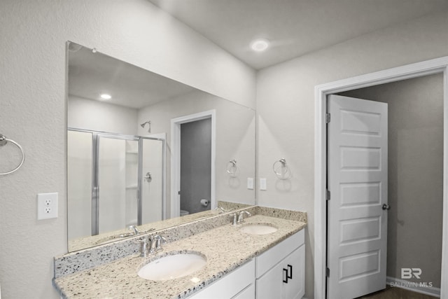 full bath featuring toilet, a sink, double vanity, and a stall shower