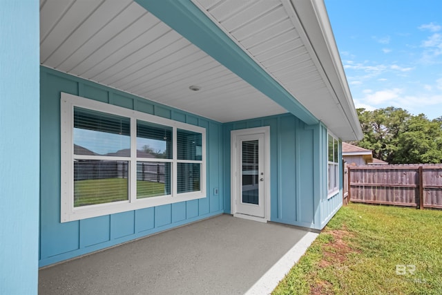 property entrance with a patio area, fence, a yard, and board and batten siding