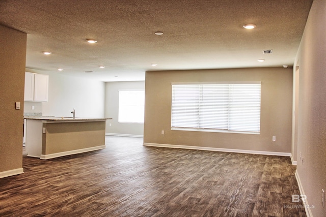 unfurnished living room with a textured ceiling, a sink, dark wood-style flooring, baseboards, and recessed lighting