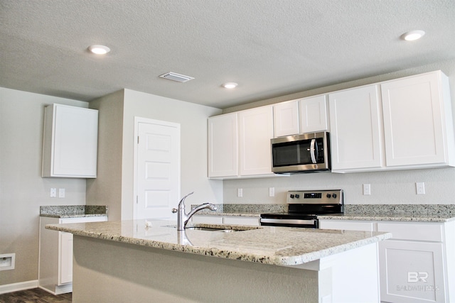 kitchen featuring a sink, an island with sink, appliances with stainless steel finishes, white cabinetry, and visible vents