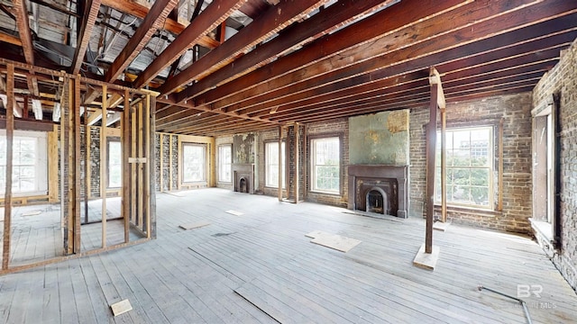 misc room featuring wood-type flooring, brick wall, and a healthy amount of sunlight