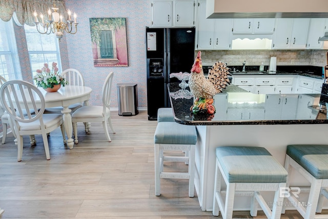 kitchen with black refrigerator with ice dispenser, white cabinetry, dark stone counters, and light hardwood / wood-style floors