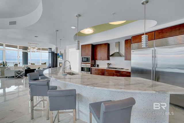 kitchen with pendant lighting, decorative backsplash, sink, built in appliances, and wall chimney exhaust hood