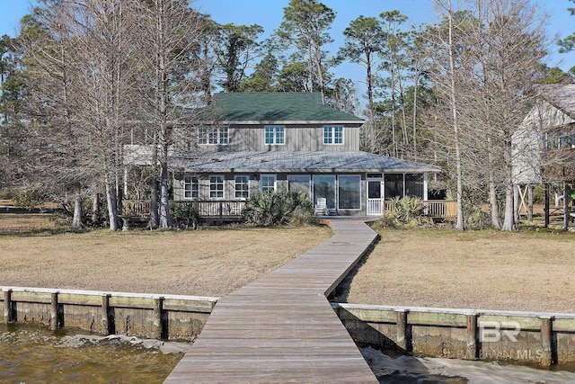 rear view of property featuring a sunroom, a water view, and a lawn