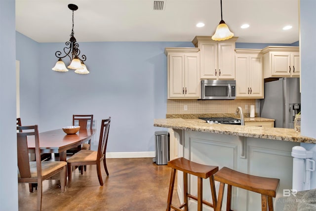 kitchen with appliances with stainless steel finishes, light stone countertops, backsplash, and a breakfast bar