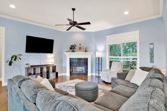 living room featuring hardwood / wood-style flooring, a tiled fireplace, ceiling fan, and ornamental molding