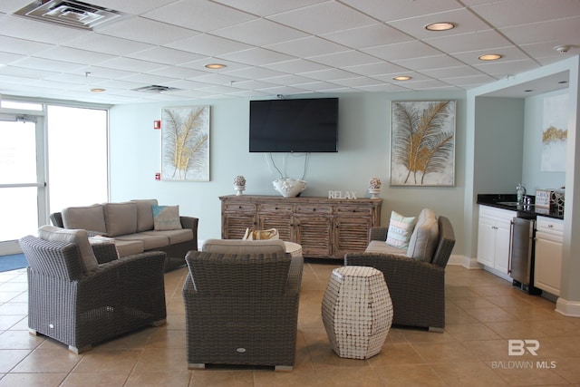 living room featuring sink, expansive windows, light tile floors, and a drop ceiling