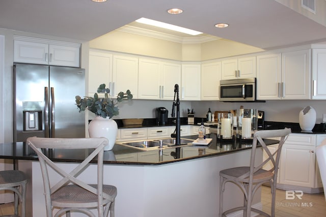 kitchen with appliances with stainless steel finishes, white cabinetry, ornamental molding, and a breakfast bar