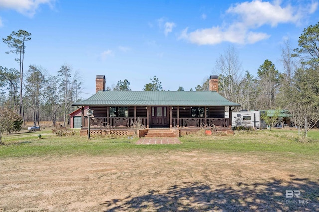 view of front facade featuring covered porch, metal roof, a chimney, and a front lawn
