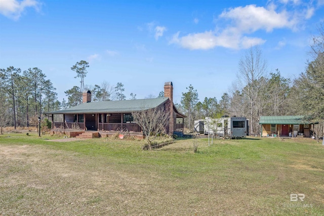 view of front facade with a front yard, covered porch, metal roof, and a chimney