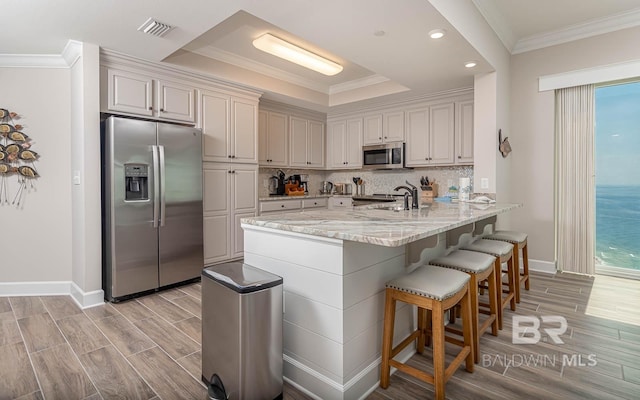kitchen featuring wood finish floors, stainless steel appliances, a peninsula, visible vents, and ornamental molding