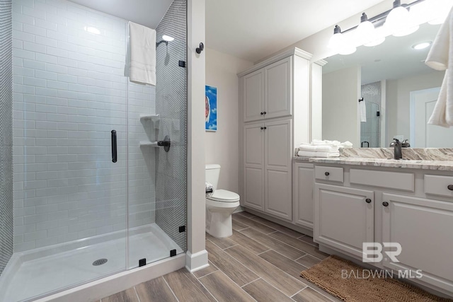 full bath featuring a stall shower, wood finish floors, vanity, baseboards, and toilet