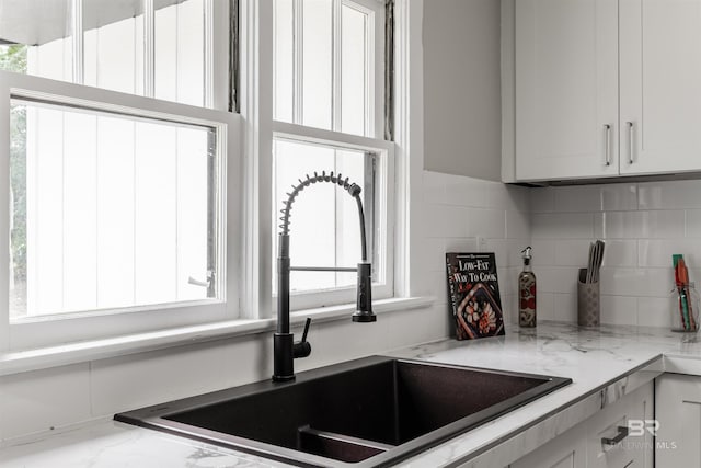 kitchen featuring white cabinetry, sink, light stone counters, and decorative backsplash