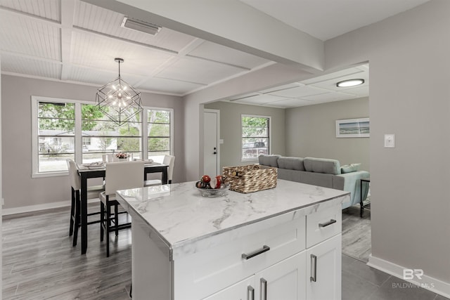 kitchen with white cabinetry, light stone counters, a center island, a chandelier, and pendant lighting