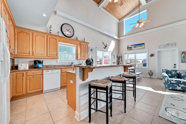 kitchen featuring white appliances, a kitchen bar, light tile patterned floors, and a wealth of natural light