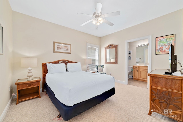 bedroom featuring light carpet, ceiling fan, ensuite bath, and baseboards