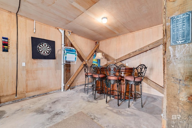 dining space featuring concrete flooring, wooden walls, and a bar