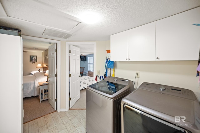 washroom with washing machine and clothes dryer, a textured ceiling, light carpet, and cabinets