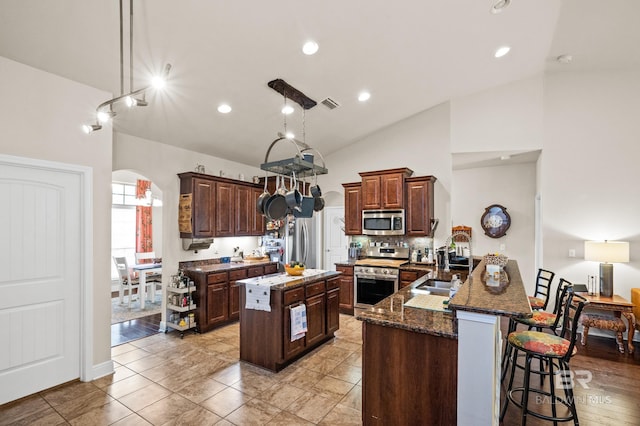 kitchen featuring stainless steel appliances, dark stone counters, vaulted ceiling, a breakfast bar, and a kitchen island