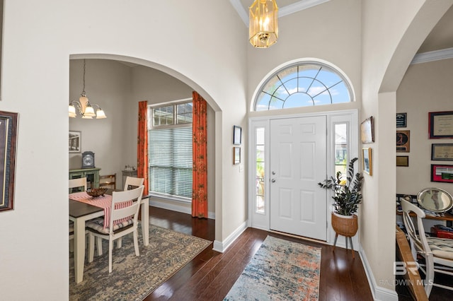 foyer with crown molding, dark hardwood / wood-style flooring, a towering ceiling, and an inviting chandelier